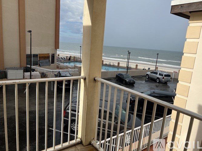 A balcony with a view of the beach and cars parked in the parking lot.