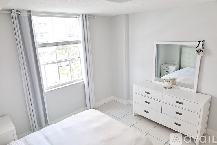 A white bedroom with a bed, dresser, and mirror.