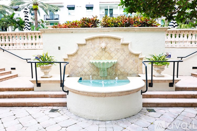 A fountain in the middle of a courtyard with a white wall and a black railing.