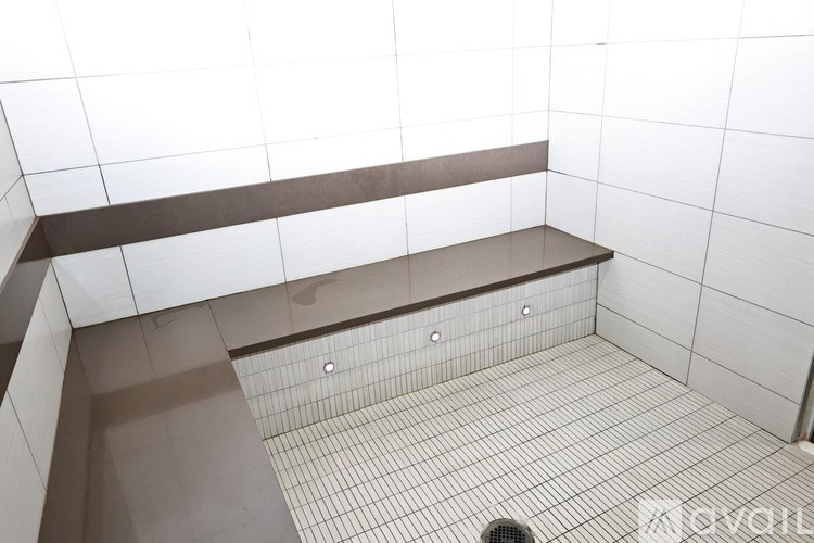 A white tiled bathroom with a brown bench.