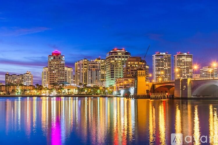 A city skyline at night with buildings reflecting on the water.