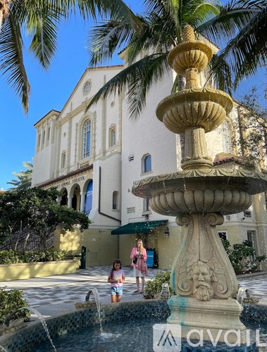 A woman in a pink dress stands next to a fountain in front of a white building.
