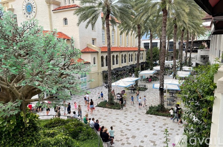 A group of people are walking around a courtyard with palm trees.