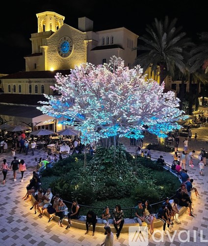 A large tree with pink and blue lights is the centerpiece of a lively outdoor gathering.