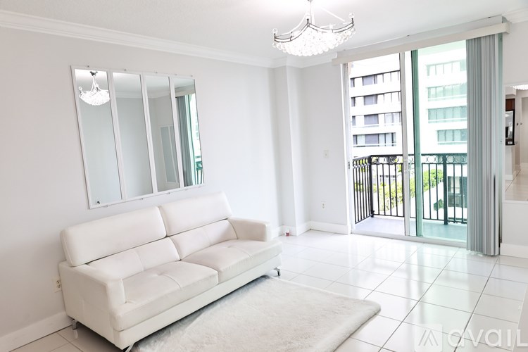 A white couch is in the middle of a bright room with a chandelier and a large mirror.