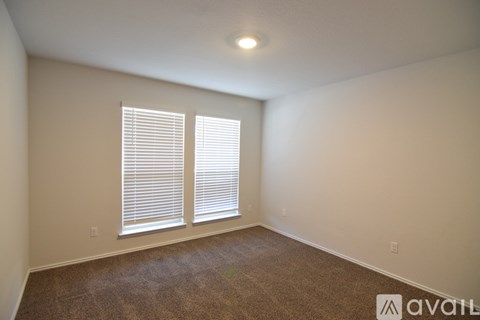 A room with a carpeted floor and two windows with blinds.