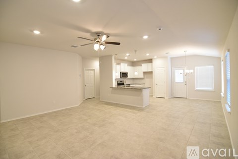 A spacious, empty room with a ceiling fan and a kitchenette in the background.