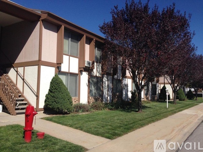 A red fire hydrant is in front of a building with a tree and bushes.