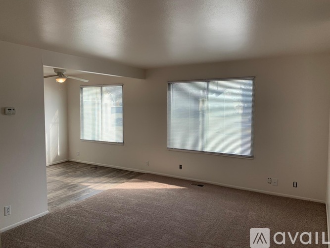 A spacious room with a carpeted floor and two windows.