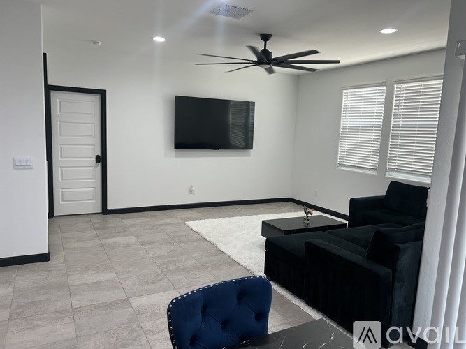 A living room with a black couch, a blue chair, and a flat screen TV mounted on the wall.