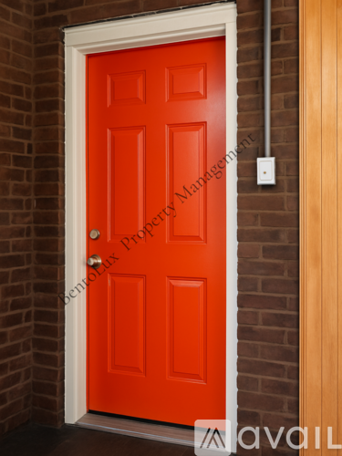 A red door with a white frame and a small white box on the wall.