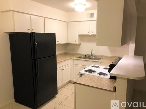A black refrigerator stands in a kitchen with white cabinets and a countertop.