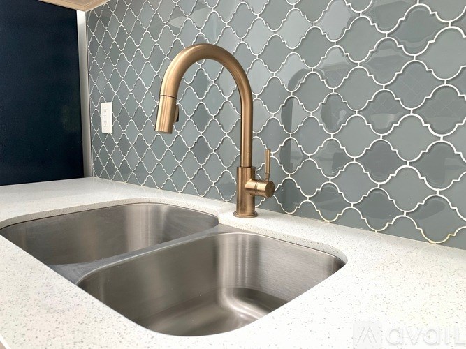 A modern kitchen sink with a gold faucet and a patterned wallpaper.