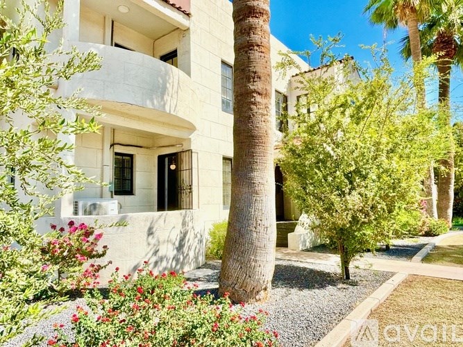 A white building with a balcony and a tree in front.