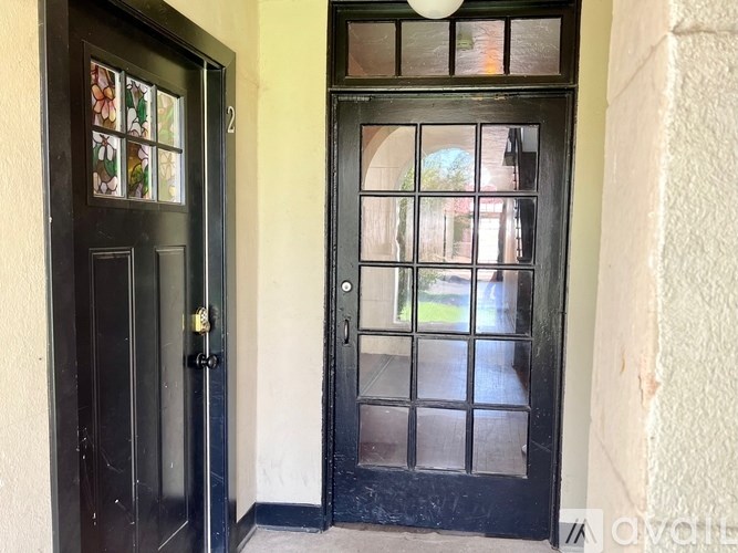 A black door with a glass window is on the right and a black door with a stained glass window is on the left.
