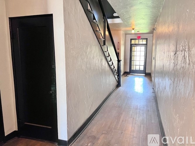 A hallway with a wooden floor and a staircase on the left side.