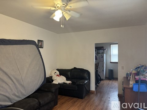 A living room with a black couch and a white teddy bear on it.