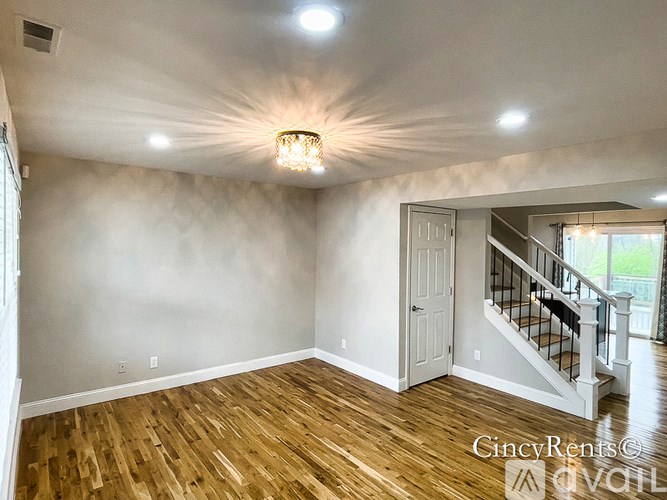 A well-lit room with wooden floors and a staircase leading to another room.