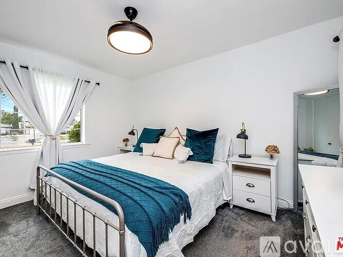 A bedroom with a bed, nightstand, and window with curtains.