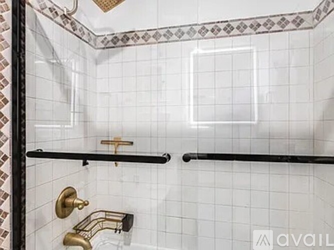 A white tiled shower with a black bar and a gold faucet.