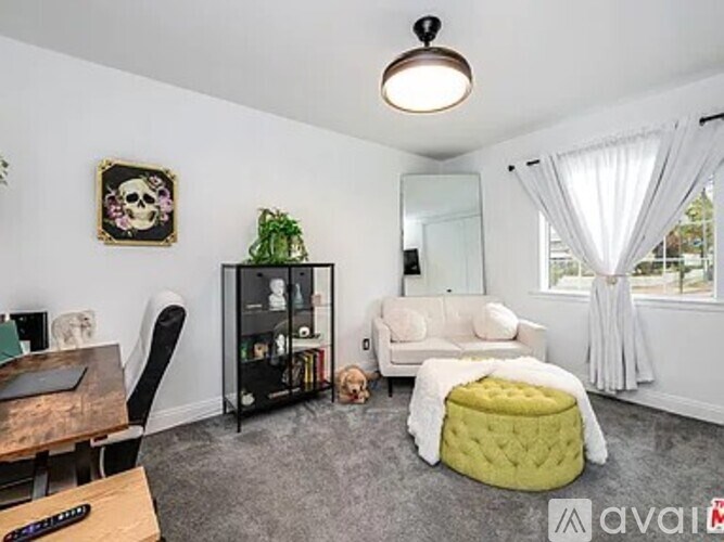 A living room with a white couch, a green ottoman, and a wooden coffee table.