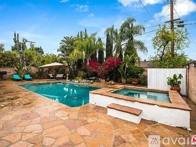 A pool surrounded by a stone patio and a white fence.