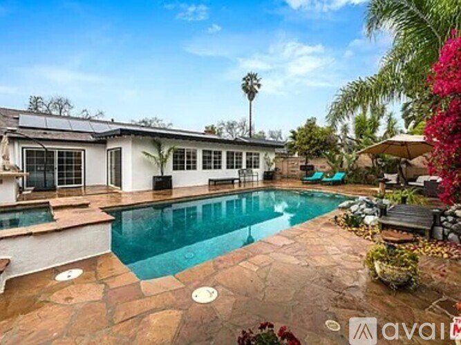 A pool surrounded by a stone patio and a house with a balcony.