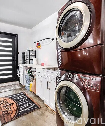 A washing machine is in the foreground of a laundry room.