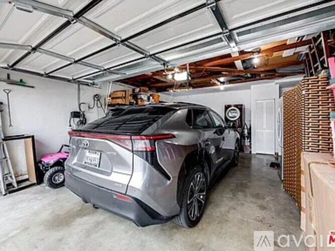 A Toyota SUV is parked in a garage with a pink toy car and a wooden structure in the background.
