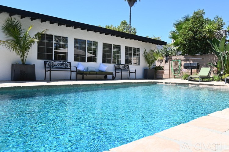 A pool in front of a house with a bench and a tree.