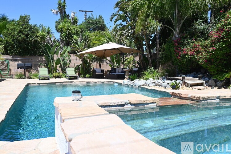 A pool surrounded by a stone wall and a patio with a table and chairs.