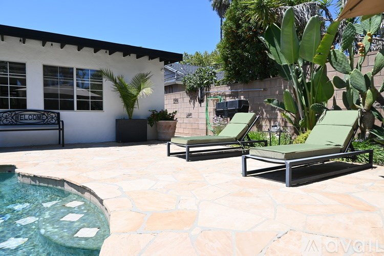 A pool with a waterfall and a patio with chairs.