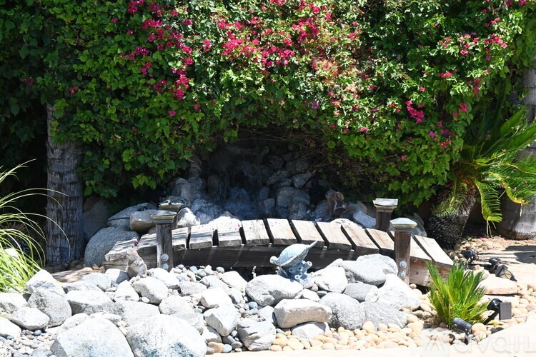 A wooden bench sits in front of a wall of greenery and flowers.