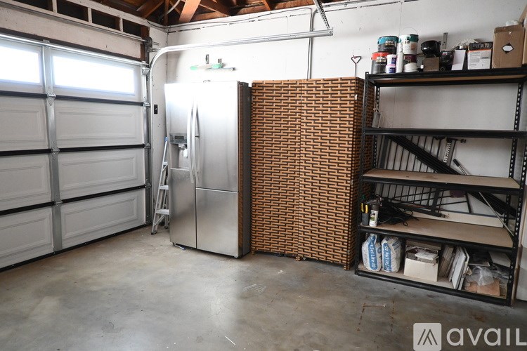 A garage with a silver fridge, a ladder, and a shelving unit.