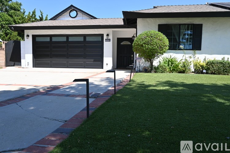 A house with a black garage door and a green bush in front.