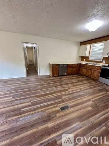 A room with wooden flooring and a kitchen area in the background.