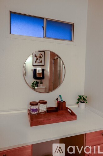 A bathroom with a round mirror and a shelf with two jars on it.