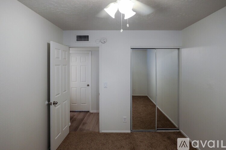 A room with a carpeted floor, a ceiling fan, and a door leading to another room.