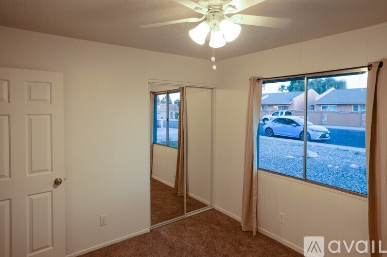 A room with a ceiling fan and a view of a street outside.