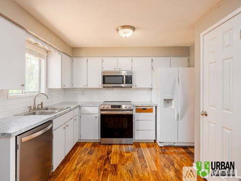 A kitchen with white cabinets and wooden floors.