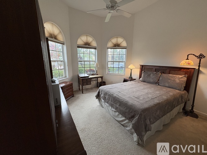 A bedroom with a large bed, a desk, and two windows with arched tops.
