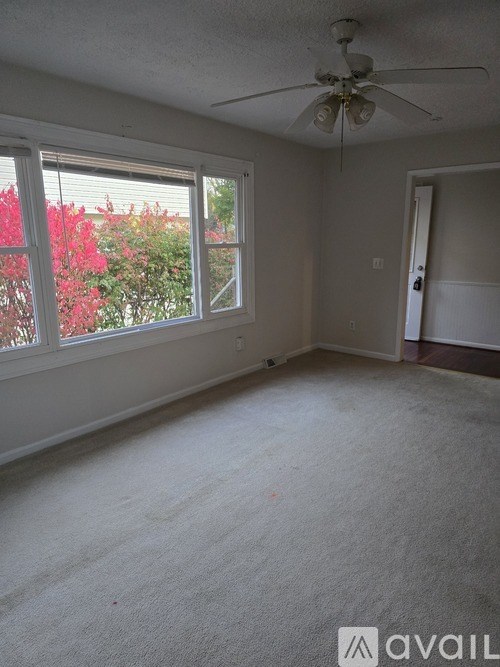 A room with a ceiling fan and a window overlooking red flowers.