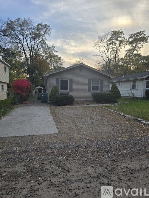 A gravel driveway leads to a house with a grey siding and a white door.