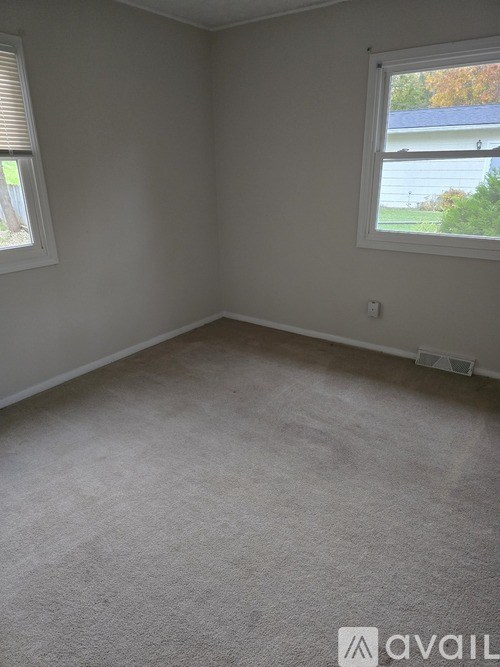 A room with a carpeted floor and two windows.