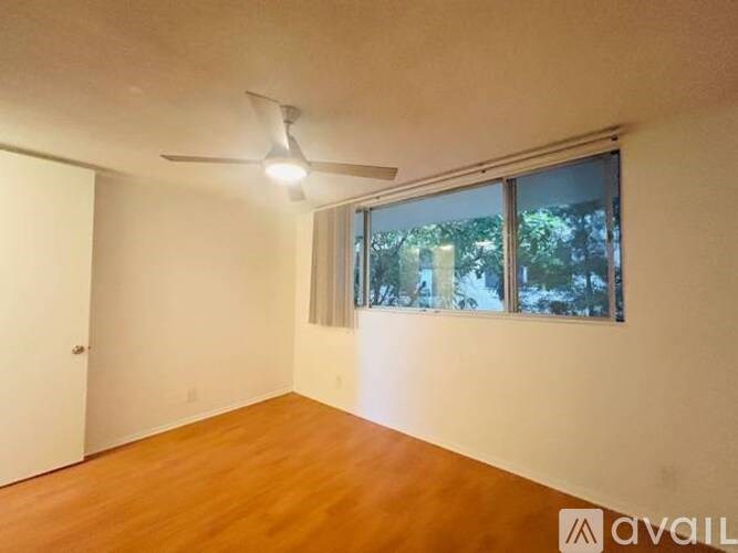 A room with a ceiling fan and a window with a view of trees outside.