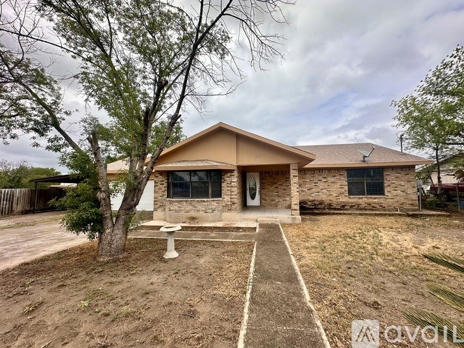 A house with a brown roof and a white door is surrounded by trees and has a concrete pathway leading to it.