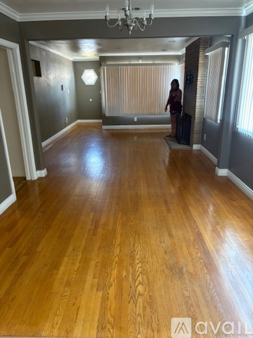 A woman is standing in a room with wooden floors and a chandelier.