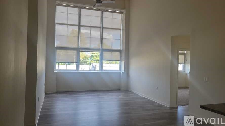 A room with a large window and wooden flooring is available for rent.