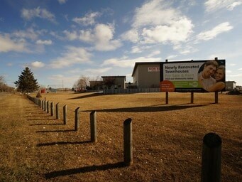 A billboard advertising newly renovated townhouses stands in a field.