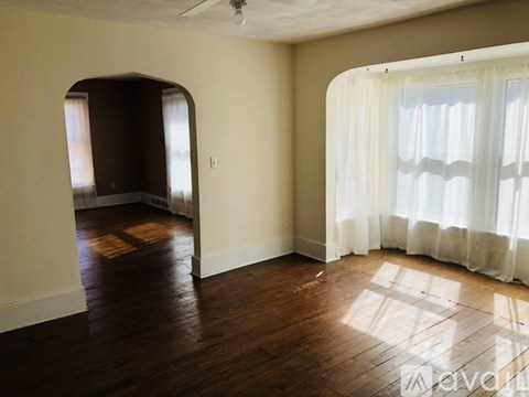A room with wooden floors and a window with white curtains.